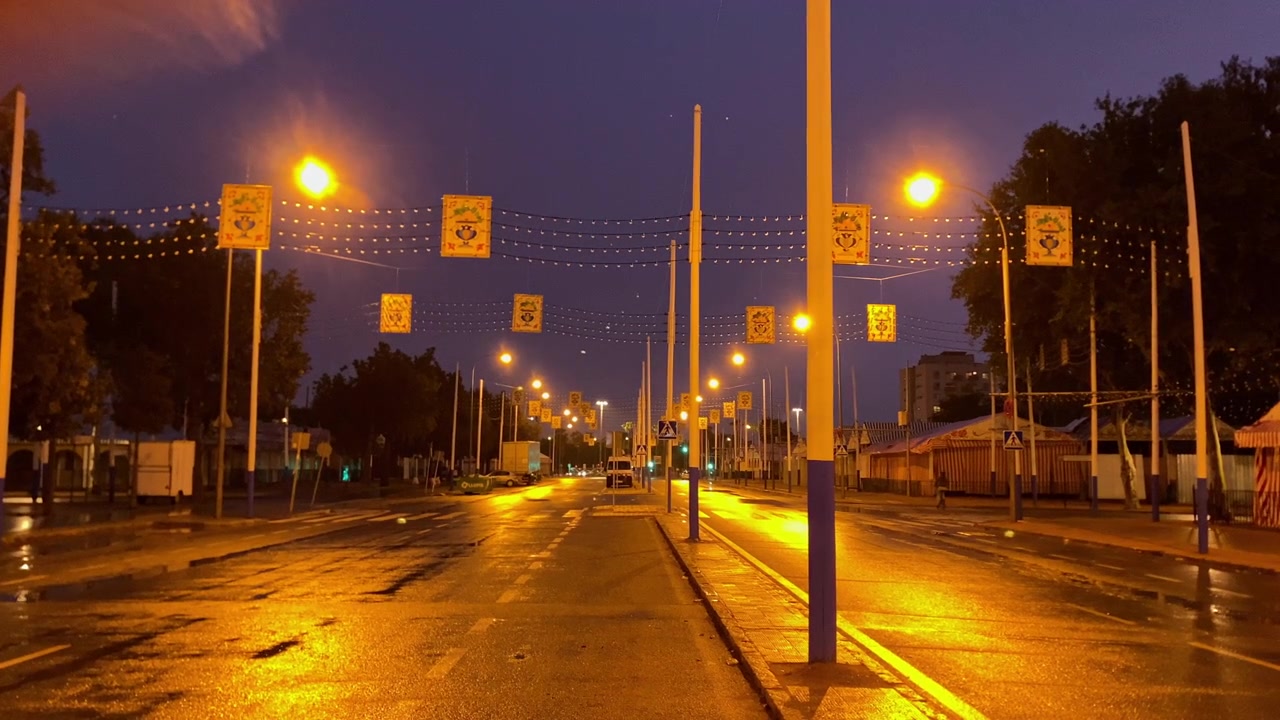 Decorações de rua com estandartes heráldicos e luzes iluminando uma estrada vazia e molhada ao crepúsculo, refletindo cores vibrantes