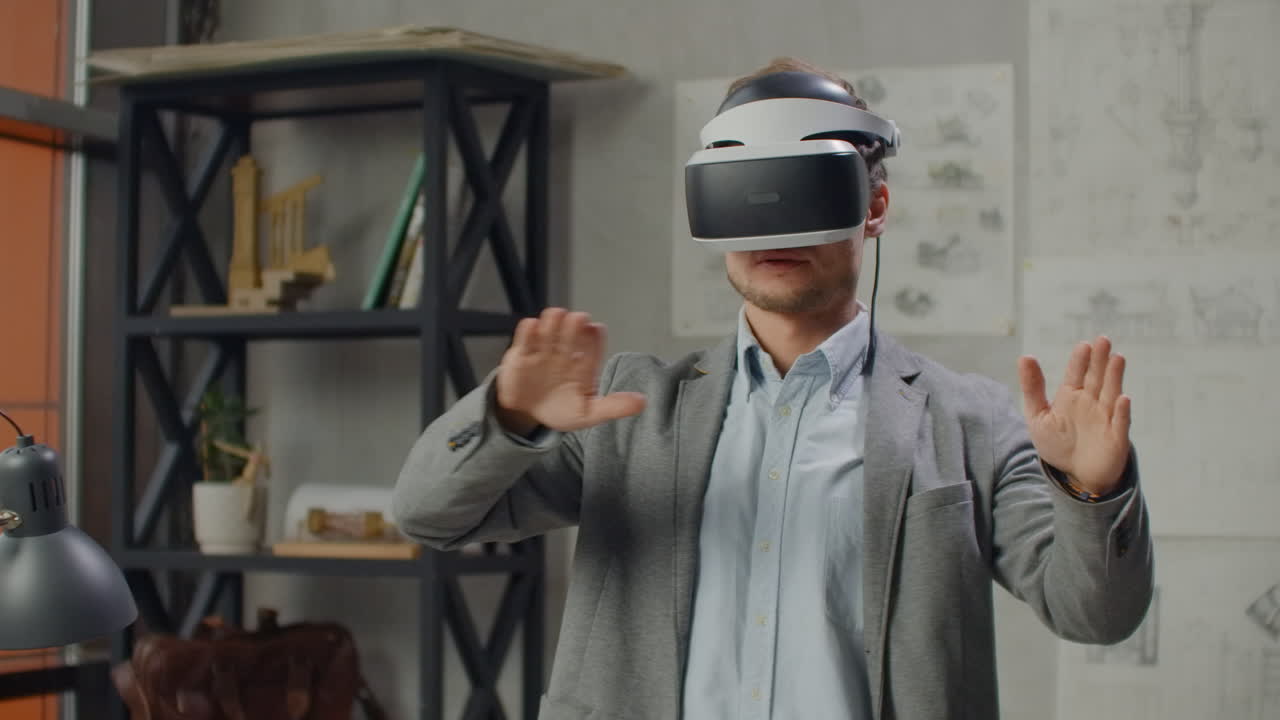 Young man designer in office in virtual reality helmet with hands makes movements imitating the work of graphic interface.