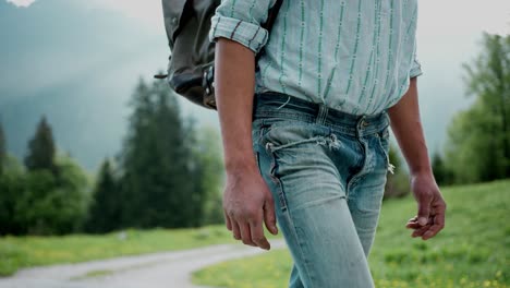 man in stylish casual street clothes and backpack hiking outdoors on mountain trail