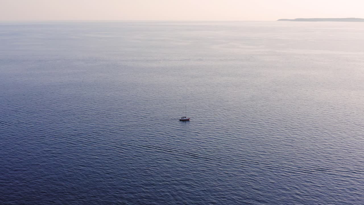 안개 낀 일몰 동안 잔잔한 바다를 가로지르는 외로운 배