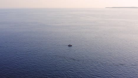 lonely boat traveling across the calm sea waters during the foggy sunset