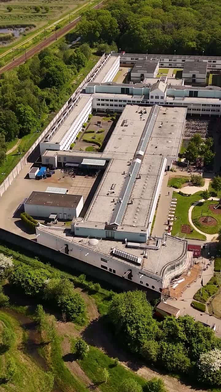 Aerial view of a large institutional building complex, possibly a prison, surrounded by green areas and railway lines