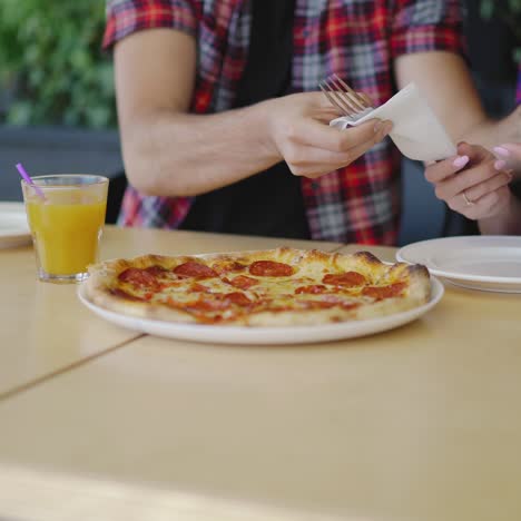 ein mann kümmert sich bei einem date um eine frau in der pizzeria. die hände eines mannes legen einen teller und besteck für eine frau.
