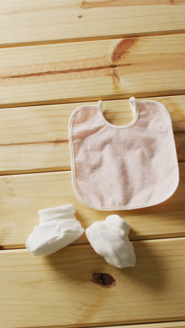 vertical video of close up of white booties and pink bib on wooden background with copy space