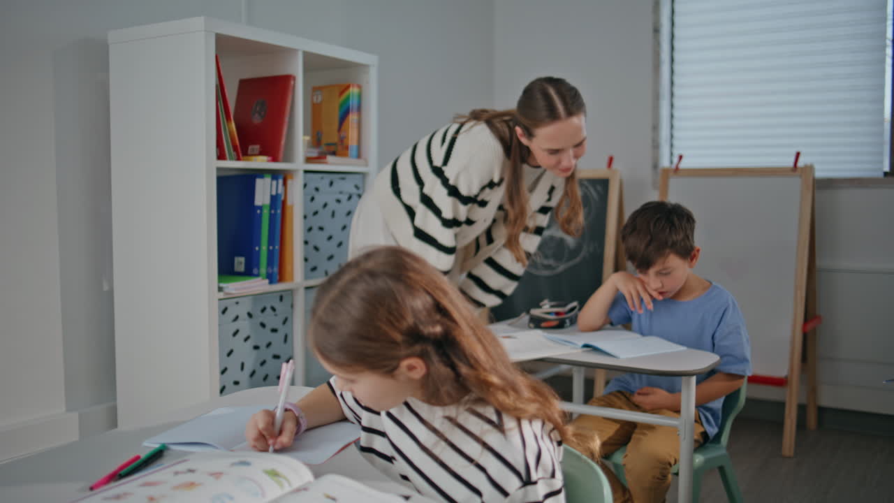 Thoughtful pupil doing class work at cabinet desk. Woman teacher helping boy