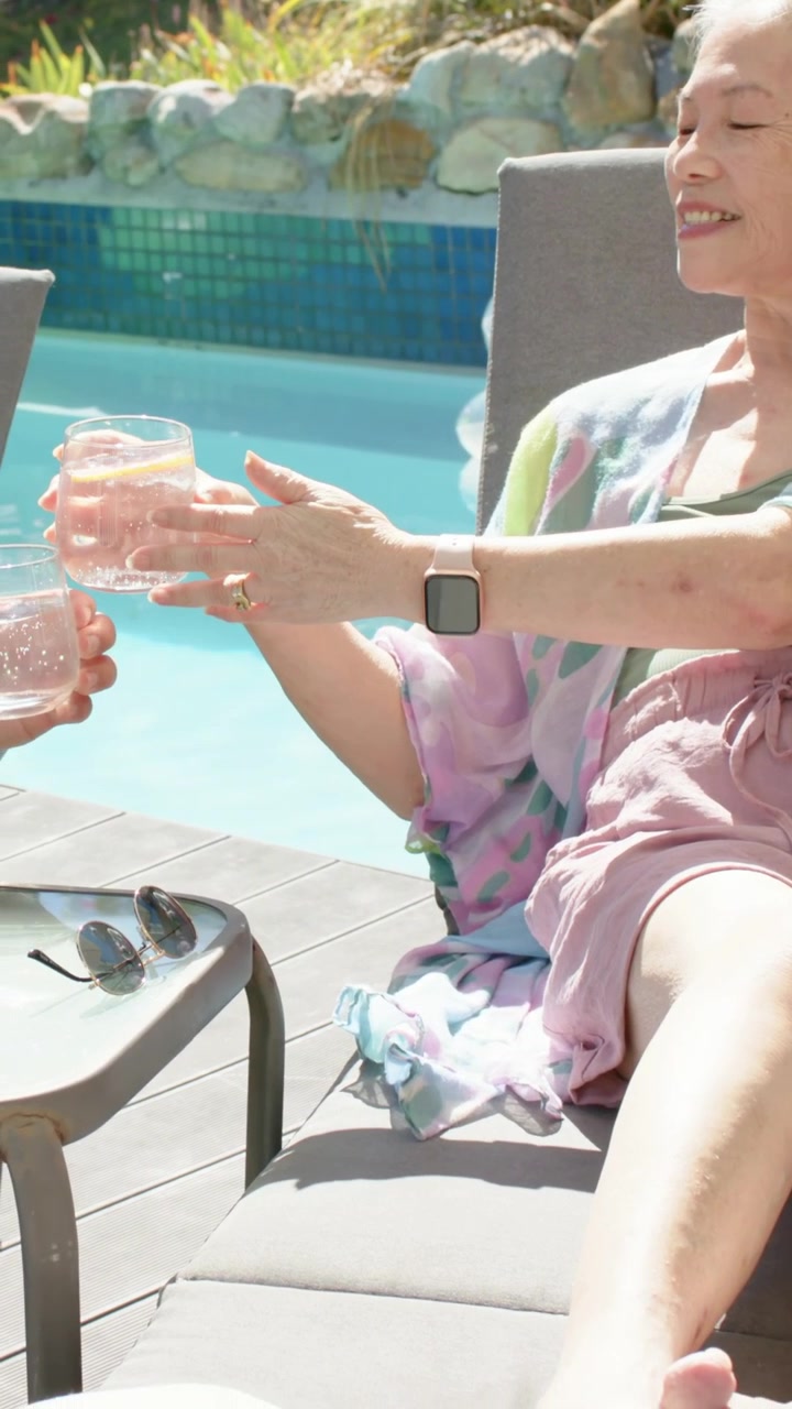 Vertical video: Reaching woman in green camisole taking drink from man offering toast poolside