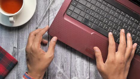 person typing on a laptop at a wooden desk with coffee