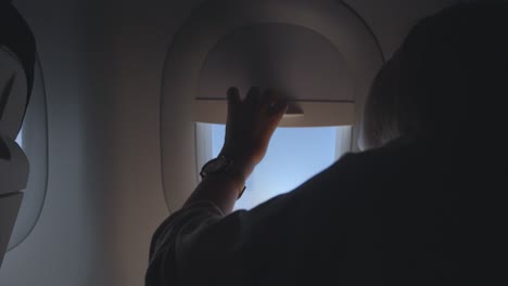 girl opens the curtain of the airplane window during flight