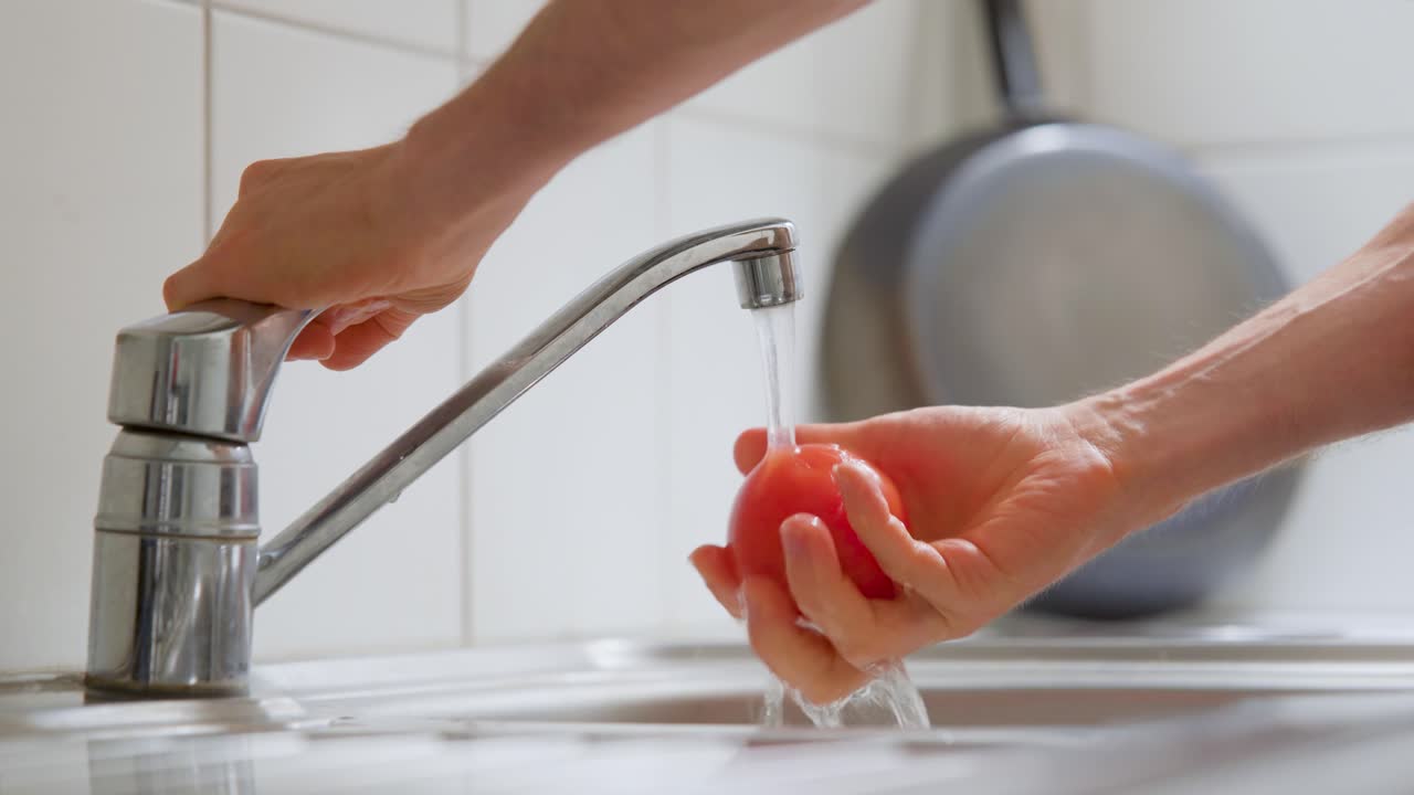Man rinsing a tomato under the kitchen faucet