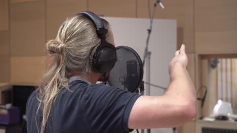 man singing to condenser mic through pop filter, recording voice, back closeup view