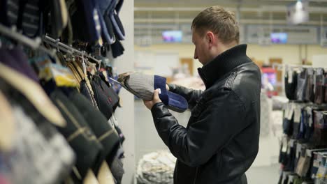 joven caucásico eligiendo zapatillas en el supermercado. seleccionando ropa cómoda para el hogar