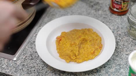 persona que coloca curry de lentejas recién cocinado en un plato blanco y pone crema encima