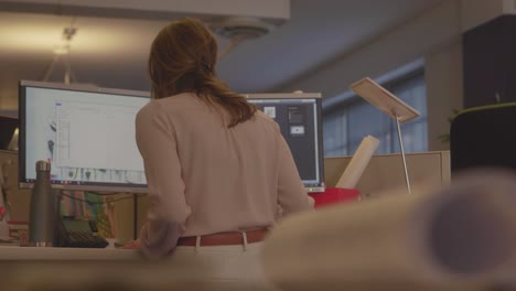 toma trasera de una mujer que trabaja frente a una computadora dentro de una oficina de arquitectura