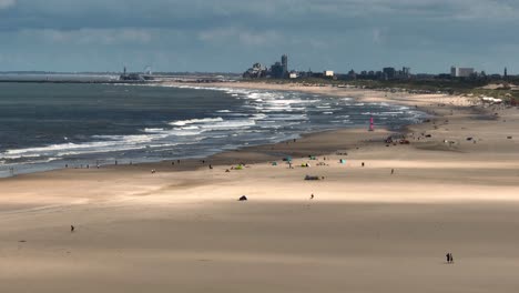 people relax on beach in overcast sunlight glow with den haag city backdrop