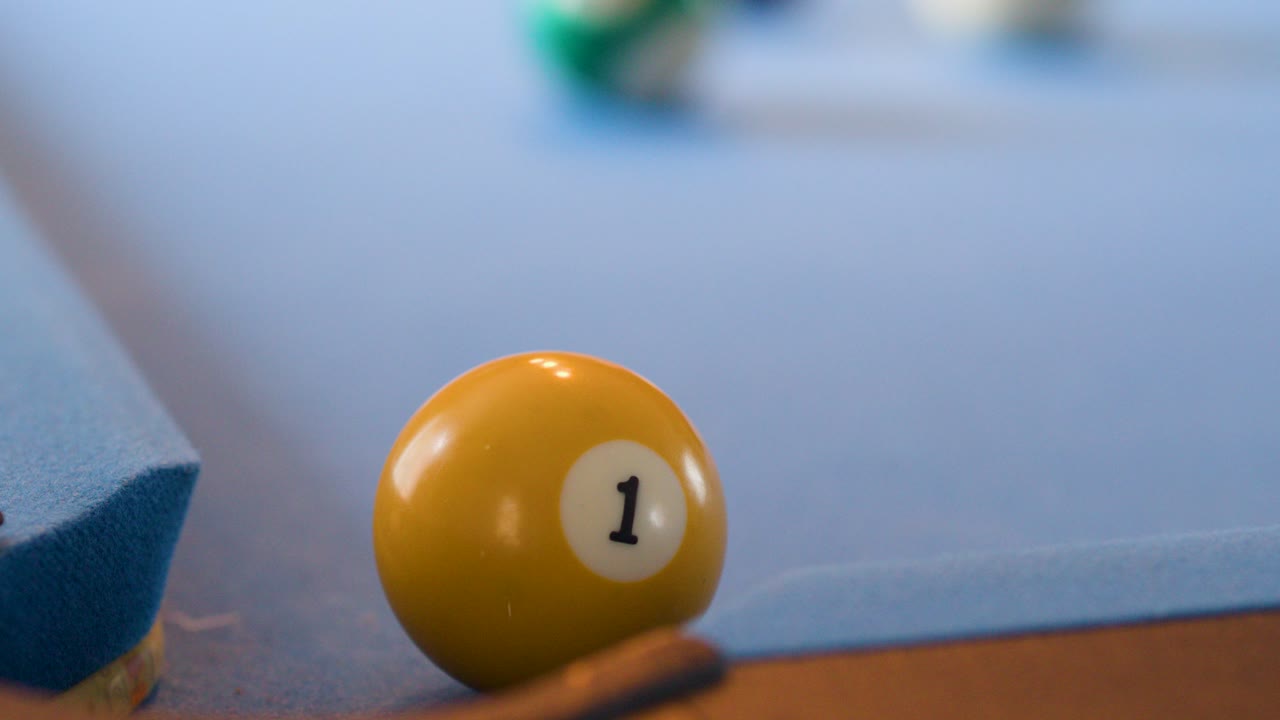 Yellow-striped ball rolls across blue felt pool table, approaching corner pocket, shallow depth of field