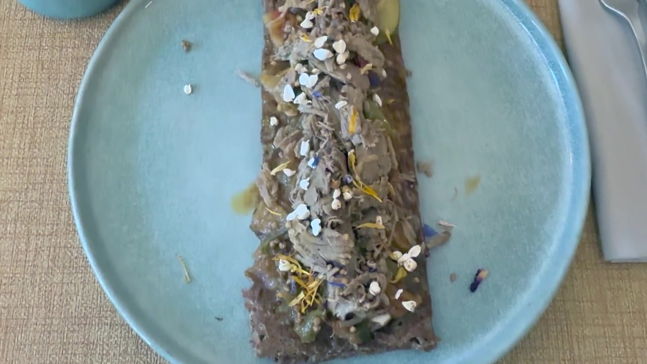 Crepe di grano saraceno elegantemente impiattata, ripiena di agnello e fiori commestibili