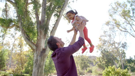 father throwing his young daughter in the air in a park