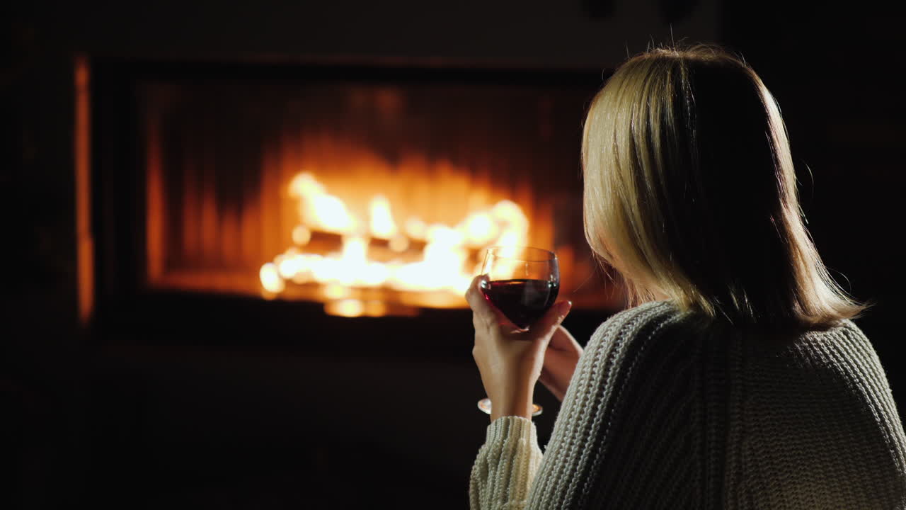 mujer bebiendo vino tinto mientras se sienta junto a la chimenea vista trasera