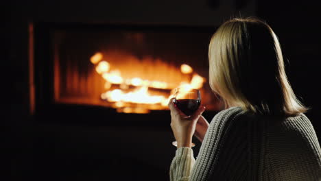 mujer bebiendo vino tinto mientras se sienta junto a la chimenea vista trasera