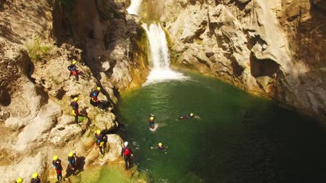 gente saltando en el río, cascada y rocas detrás