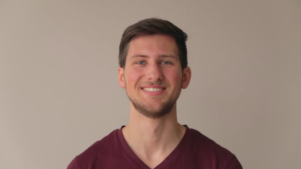 joven modelo masculino riendo y sonriendo frente a la cámara, todavía filmado en un primer plano medio