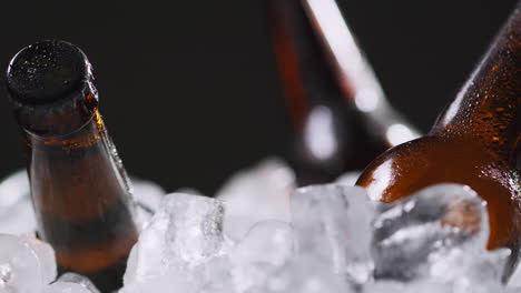 cerrar las botellas de vidrio de cerveza fría o refrescos que se enfrían en un cubo lleno de hielo contra un fondo negro 2