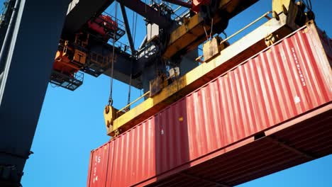 a heavy red shipping container suspended from a crane against a clear blue sky, showcasing the industrial power and precision of modern cargo handling operations