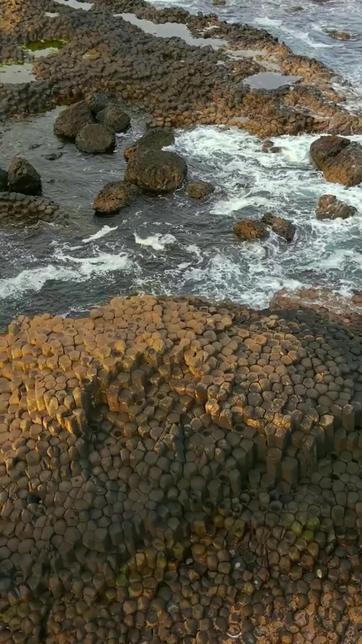 Video aereo dall'alto in senso orario con rapporto verticale per social media del Selciato del Gigante a Bushmills, Contea di Antrim nell'Irlanda del Nord, Regno Unito. Prodotto in formato verticale 1080x1920 con colori Rec709.