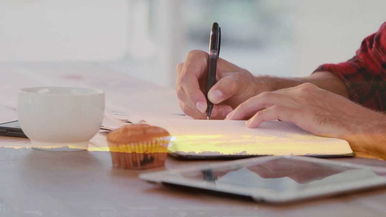 Camera pulling back, revealing red plaid hands placing pen and writing notes in notebook for study