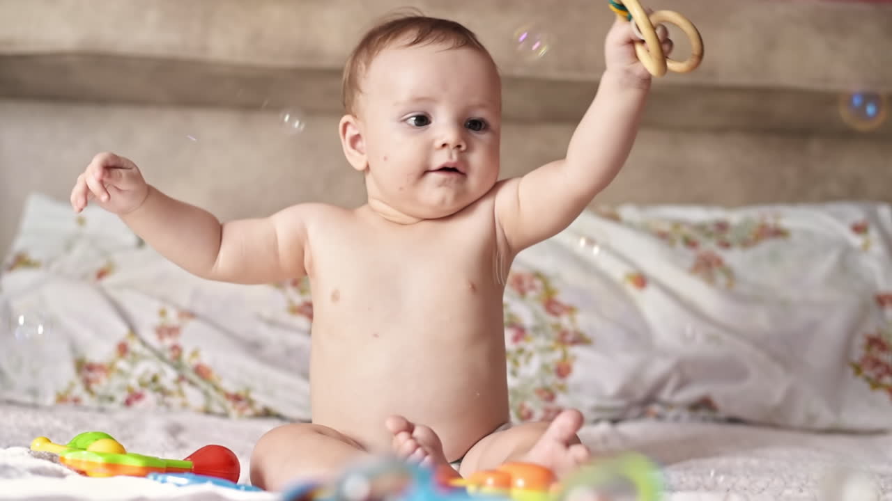 Caucasian blonde baby boy on a bed, playing with toys. Soap bubbles flying around