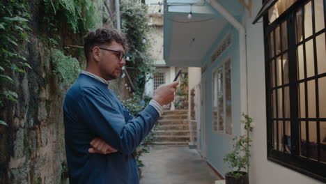 young man standing outside of house and using smartphone