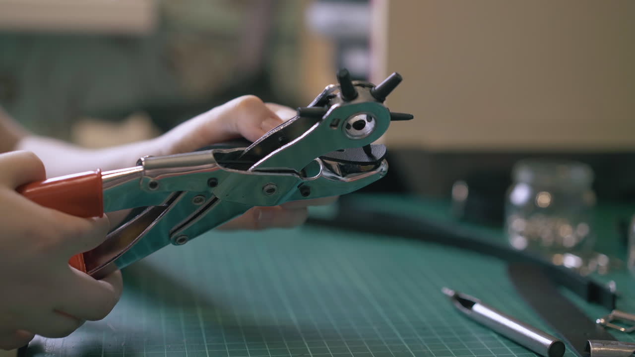 el diseñador hábil hace un agujero en el cinturón de cuero negro con un puñetazo