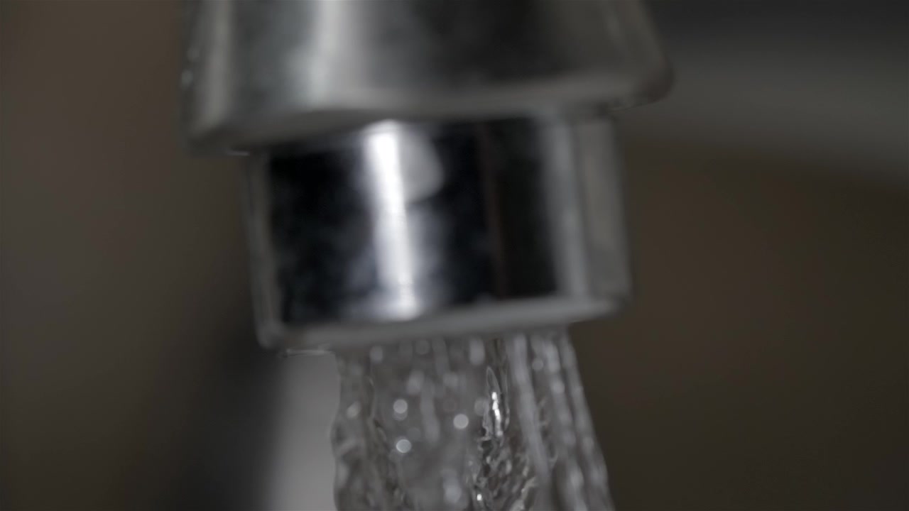 Primo piano di un rubinetto metallico con getto d'acqua corrente, concetto di tubazione.