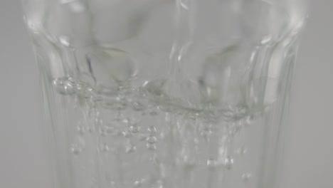 slowmotion macro of still water pouring into clear glass in front of neutral background