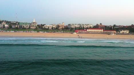 Stationäre-Drohnenaufnahme-Von-Bondi-Beach-über-Dem-Wasser,-Während-Ein-Rettungsschwimmer-Buggy-Am-Strand-Entlang-Fährt,-Sydney,-Australien