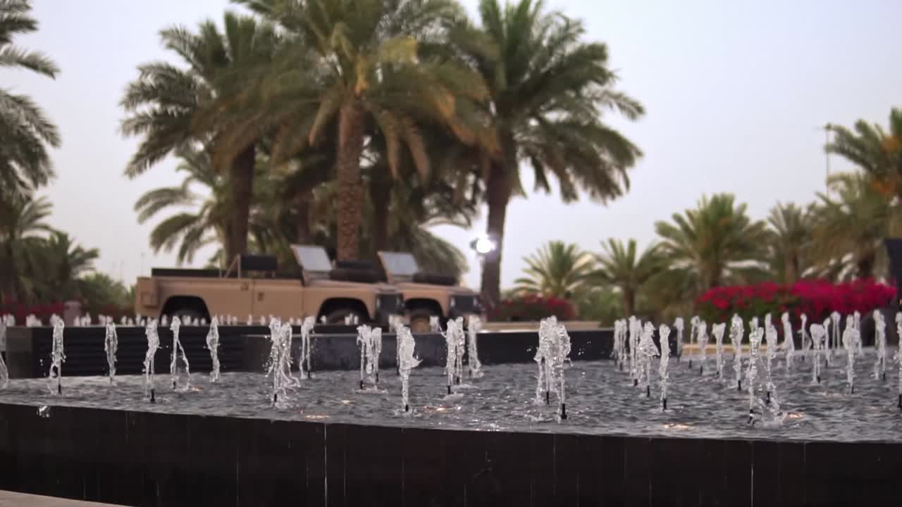 A Majestic water fountain near the Sheikh Zayid Grand Mosque with a Miltary-styled jeep and date palm tree garden in the background