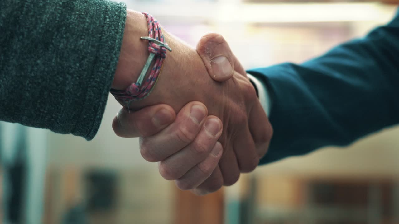 Close-up view of a permissive handshake between two people in casual businesslike clothing