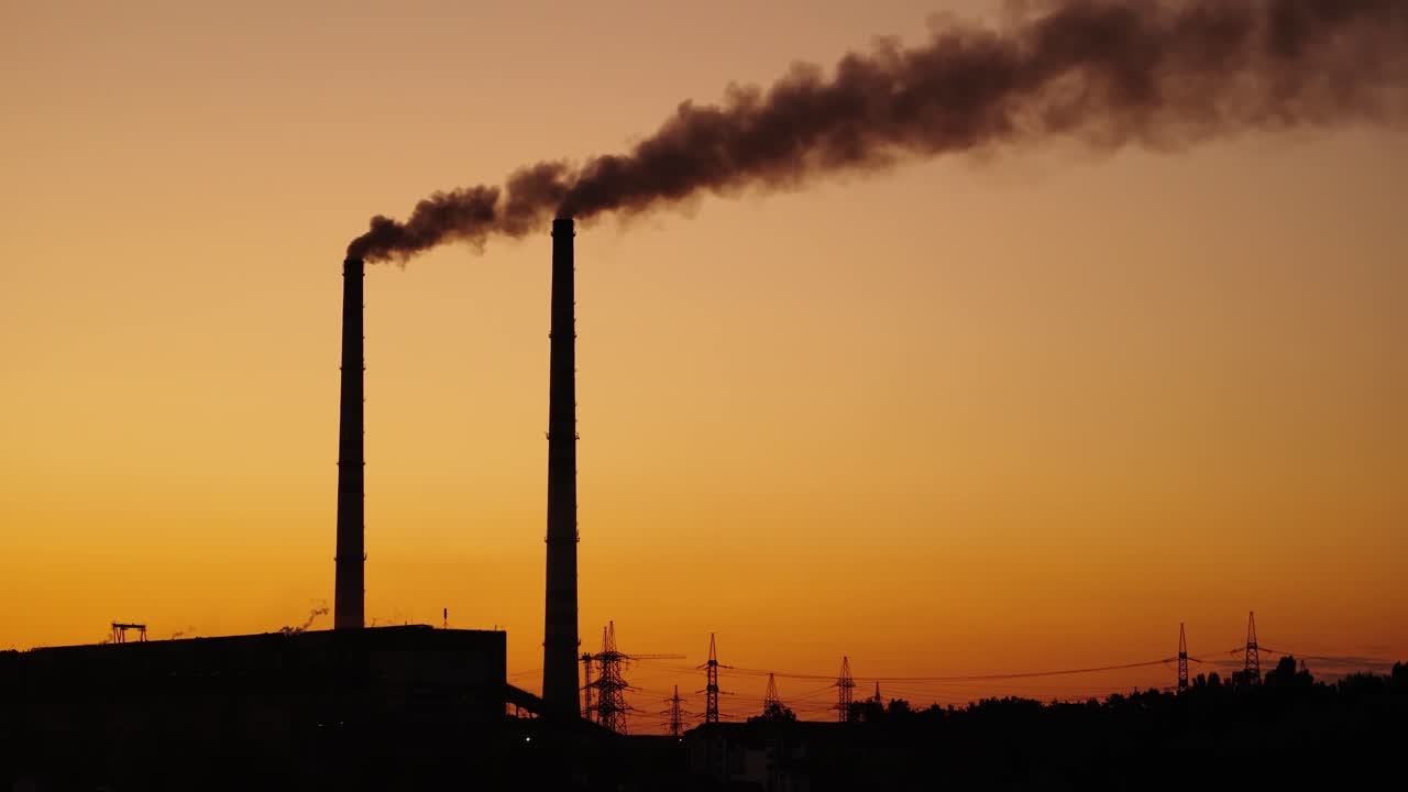 Dark pipes with emissions on the orange sky background. Dirty smoke coming from industrial pipes into the air at sunset. Pollution the environment.