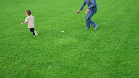 little toddler boy waves his hand and throws a ball. grandpa and grandson playing happily outdoors.