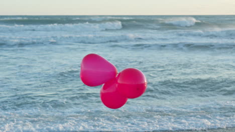 tres globos rojos bailan en el viento mientras las olas del mar rompen en el fondo