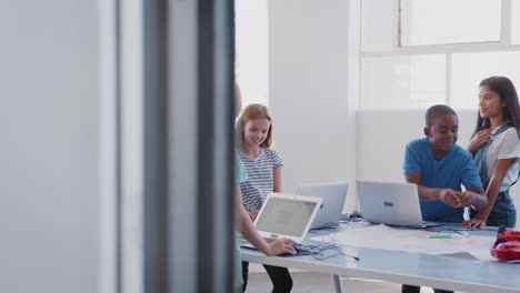 Estudiantes-Con-Profesora-En-Clase-De-Codificación-Informática-Después-De-La-Escuela-Aprendiendo-A-Programar-Vehículos-Robot