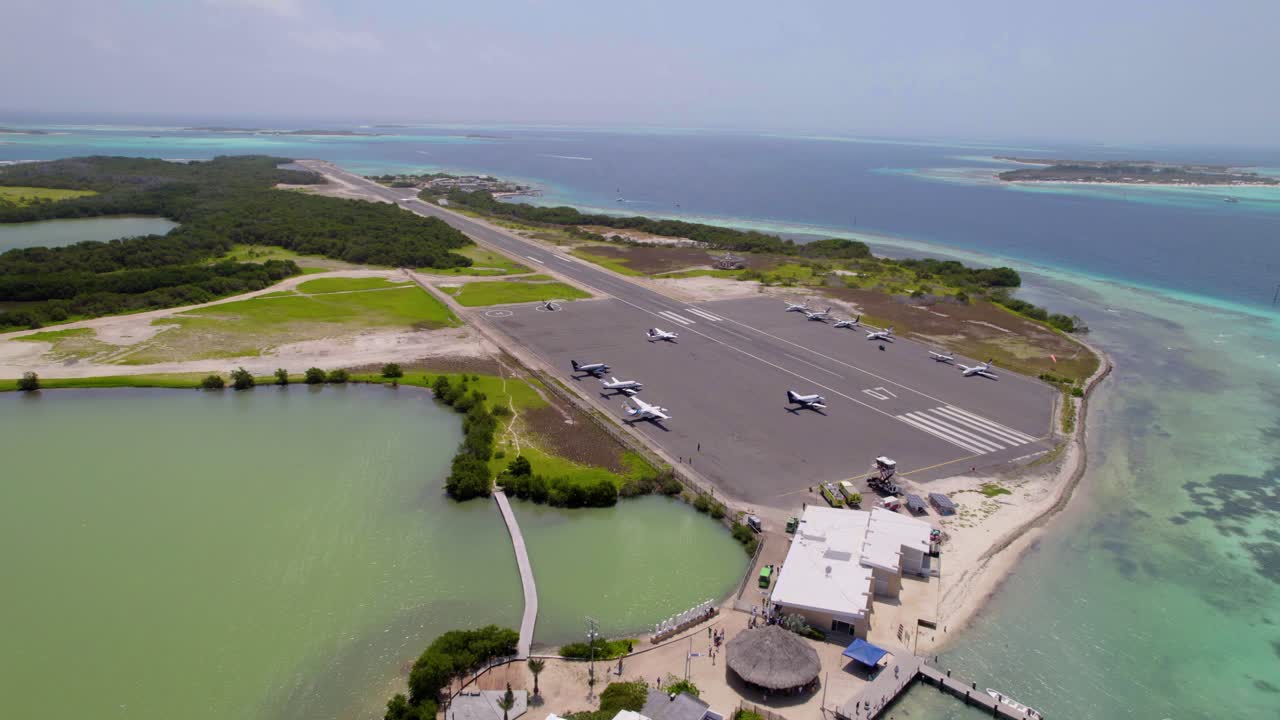 Aerial drone rising over Los Roques airport, showing small planes, lagoon, boats, and Caribbean Sea in Venezuela.