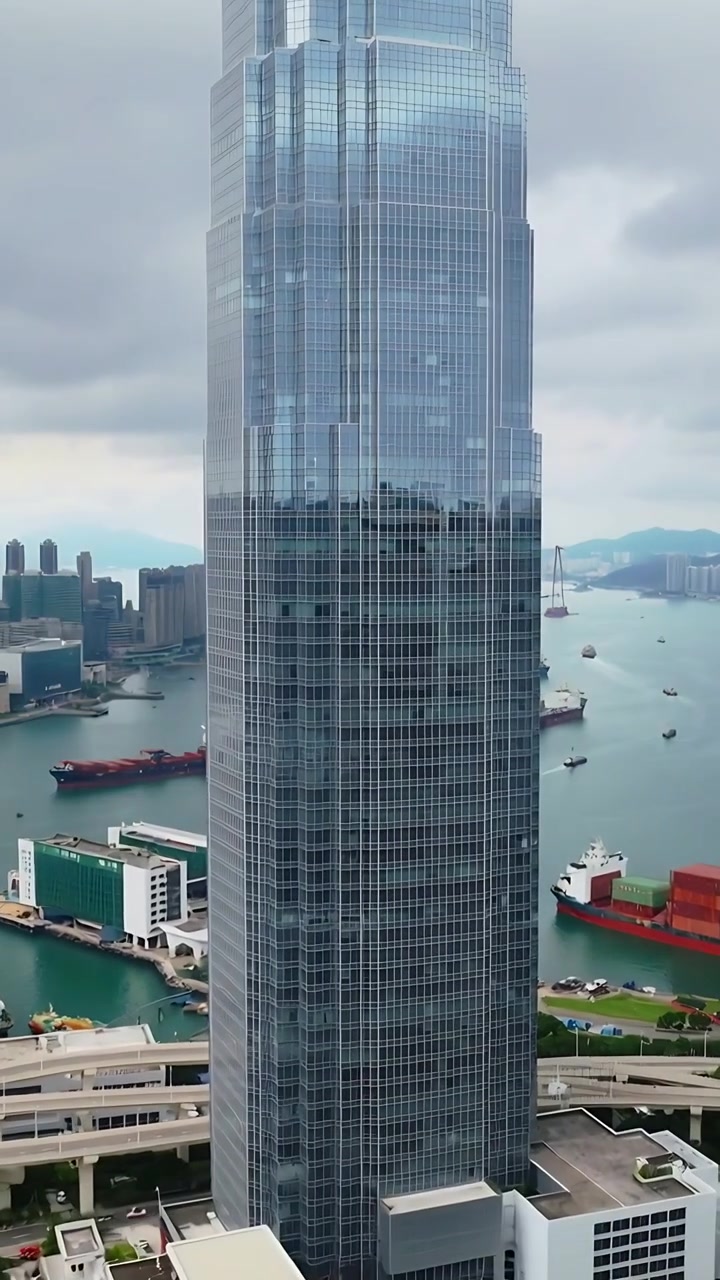 Vídeo vertical: Câmera inclinando, revelando torre de vidro de uma varanda, mostrando navios de carga e rodovia