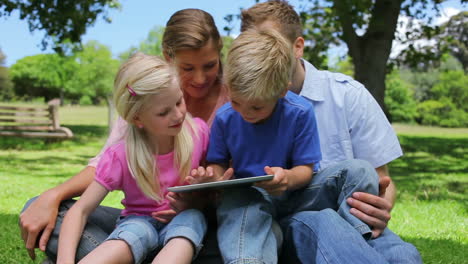 Familia-Sentada-Junta-Mientras-Usa-Una-Tableta-En-Un-Parque