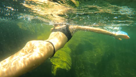 slow motion pov of woman swimming underwater in rocky river during sunny day ,4k following shot