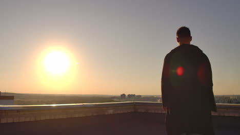 The-camera-follows-a-man-walking-across-a-rooftop-at-sunset-with-a-laptop-and-a-bottle.-The-freelancer-opens-the-laptop-and-types-on-the-keyboard.-Slow-motion-hacker-walks-on-the-roof-with-a-laptop.