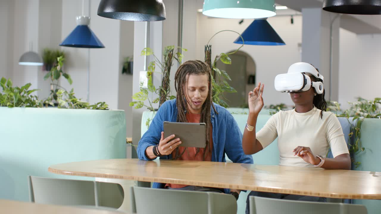 African American pair testing white VR headset woman lifting hand as man guiding tablet at table