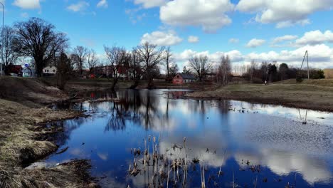 Aerial-drone-fly-above-skyline-reflected-on-water-around-european-village-in-autumn,-dry-trees-and-houses