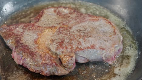 entrecote bistec en sartén, tapa roja cruda girada hacia el fuego, lado marrón visible después de girar, primer plano, 60 fps