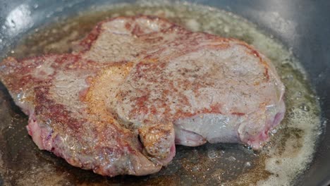 entrecote steak in pan, raw red top turned to sear, browned side visible after turning, closeup, 60 fps